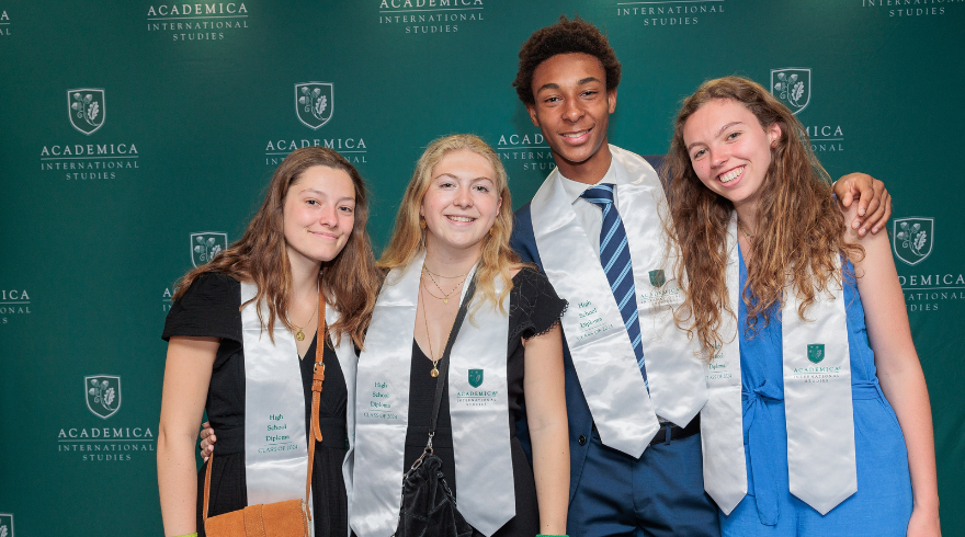 Quatre jeunes diplômés Dual Diploma souriants posent devant un fond vert marqué du logo et du texte 'Academica International Studies'